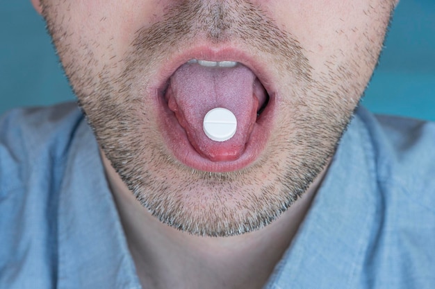 Biorąc białą tabletkę z bliska młody człowiek biorący leki na ból