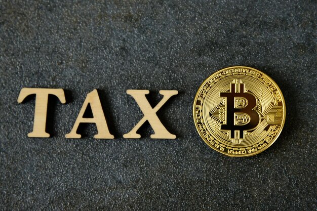 Bitcoin i obok drewniane z literami TAX. Koncepcja opodatkowania Bitcoin. Moneta bitcoin Crypto Currency Z komunikatem TAX ,Koncepcja określenia prawa podatkowego pieniądza cyfrowego