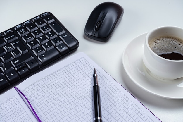Zdjęcie biurko biurkowe. obszar roboczy z pustą książką notatek, klawiaturą, artykułami biurowymi i filiżanką kawy na białym tle.
