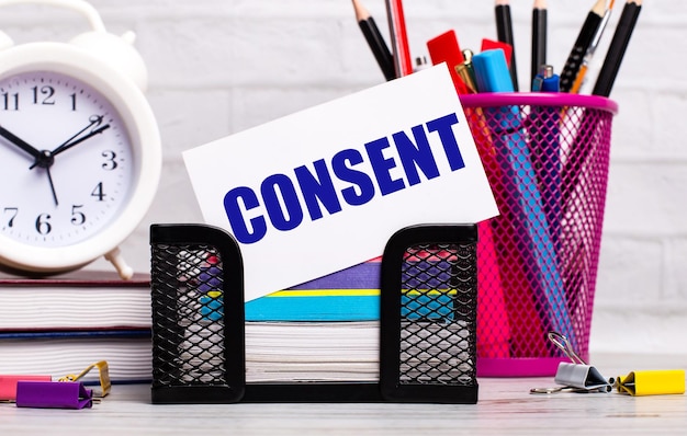 Biurko ma pamiętniki, papeterię z budzikiem i białą kartę z tekstem CONSENT Business concept