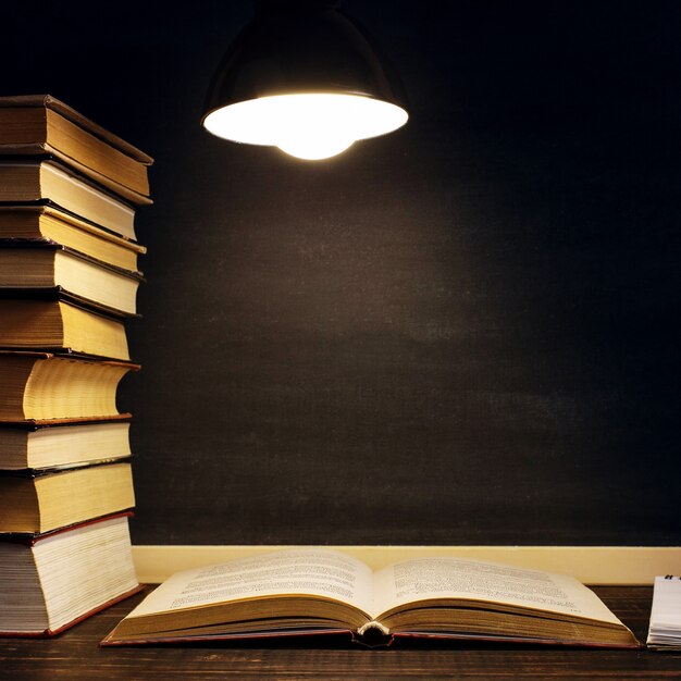 Zdjęcie biurko na tle tablicy kredowej, książki w ciemności w świetle lampy.