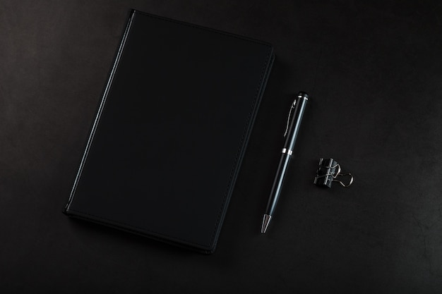 Biurko z czarnym notatnikiem i długopisem na czarnym tle. Widok z góry z miejscem na kopię. Cele biznesowe i koncepcja założeń