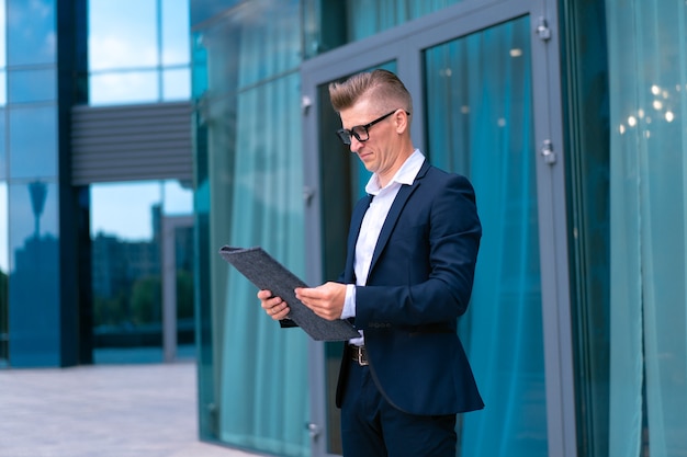 Biznes. Biznesmen okulary z folderem stojący budynek biurowy wejście przystojny kaukaski mężczyzna biznes osoba portret miasto korporacyjny budynek tło udany młody dorosły kierownik