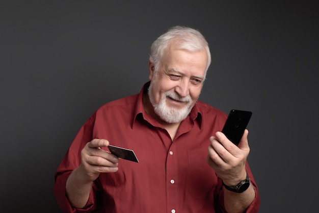 Biznes, grizzled mężczyzna trzyma kartę bankową i telefon i uśmiechnięty