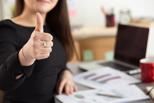 Biznes kobieta pokazuje kciuk siedzący w jej biurze zbliżenie. Idealna koncepcja jakości towarów lub usług