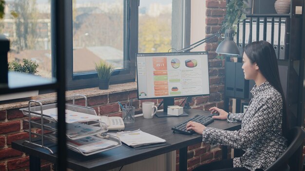 Biznes kobieta przy użyciu komputera do planowania strategii marketingowej w biurze uruchamiania. Przedsiębiorca pracujący z rocznymi wykresami danych w celu opracowania projektu i prezentacji finansowej. Rozwój branży