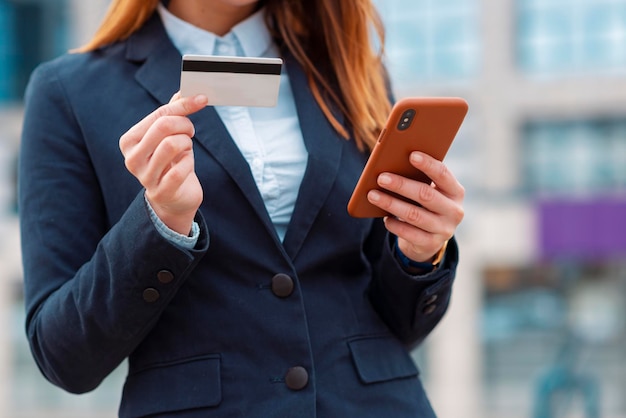 Zdjęcie biznes kobieta trzymająca kartę kredytową i telefon na zewnątrz