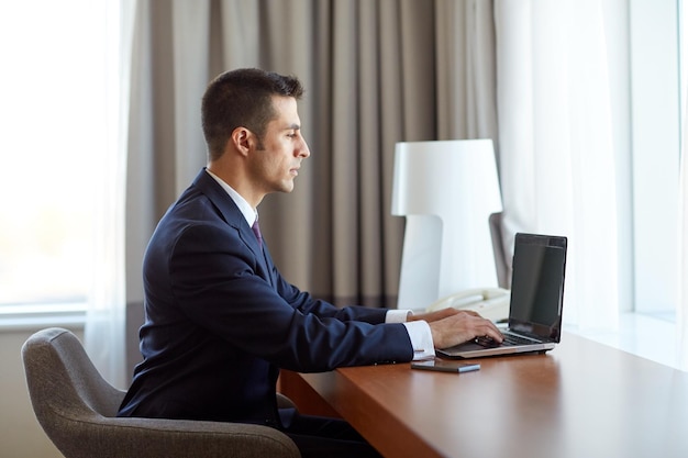 Biznes, ludzie i koncepcja technologii - biznesmen piszący na laptopie w pokoju hotelowym