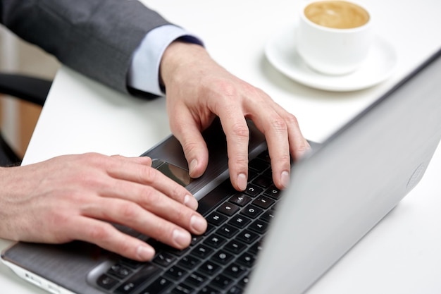 biznes, ludzie i koncepcja technologii - zbliżenie męskich rąk z laptopem i filiżanką kawy w biurze