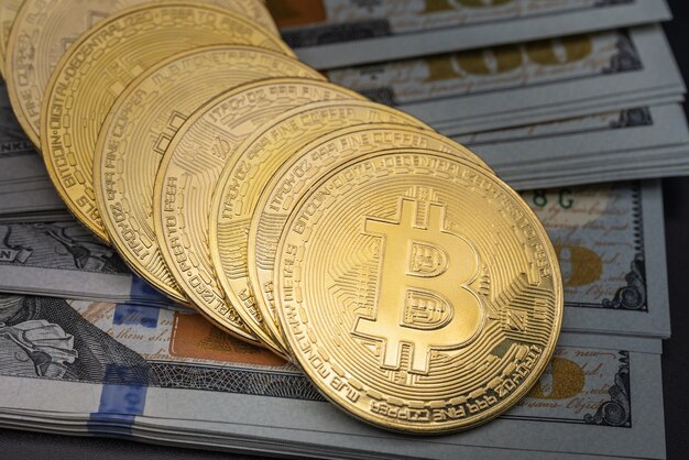 Biznes, pieniądze, technologia i koncepcja kryptowaluty. Zbliżenie złotych monet bitcoin na stosie banknotu 100 dolarów amerykańskich.