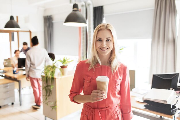 Zdjęcie biznes, startup i koncepcja ludzi - szczęśliwa bizneswoman lub kreatywna kobieta z filiżanką kawy w biurze