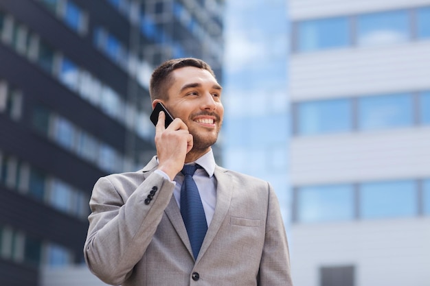 Biznes, technologia i ludzie pojęć, - uśmiechnięty biznesmen opowiada nad budynkiem biurowym z smartphone