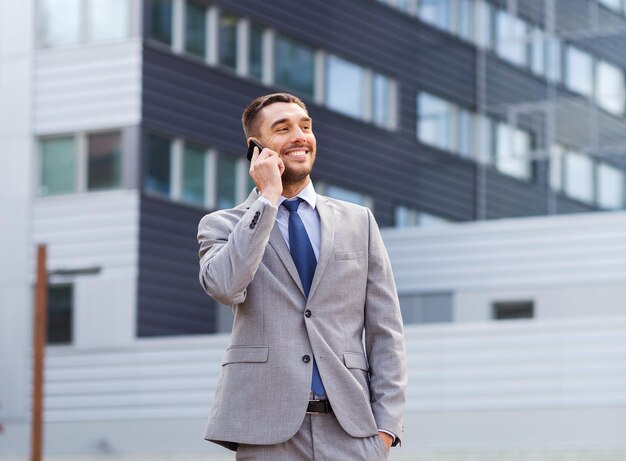 Biznes, technologia i ludzie pojęć, - uśmiechnięty biznesmen opowiada nad budynkiem biurowym z smartphone