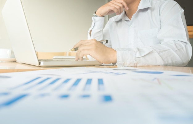 Biznesmen analizujący wykresy i używający laptopa przy biurku