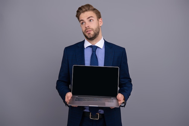 Biznesmen biznesmen w garniturze pokazujący laptop prezentujący produkt biurowy izolowany na szarym