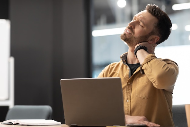 Biznesmen dotykający ból szyi za pomocą laptopa w biurze