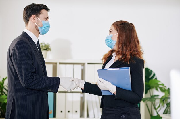 Biznesmen I Bizneswoman W Medycznych Maskach I Rękawiczkach, ściskając Ręce Podczas Witania Się Przed Spotkaniem
