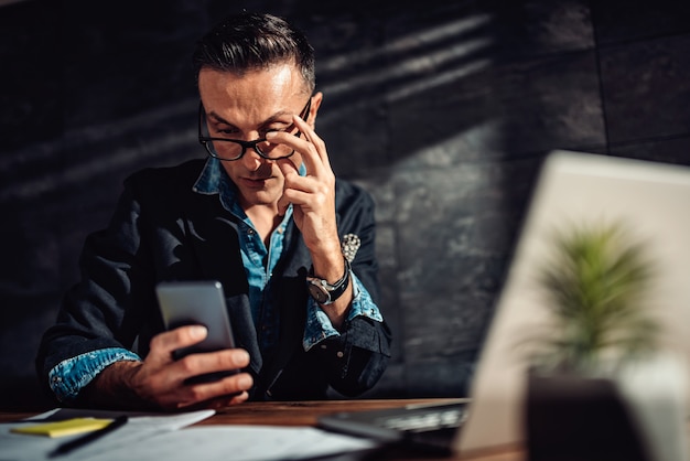 Biznesmen jest ubranym eyeglasses używać mądrze telefon