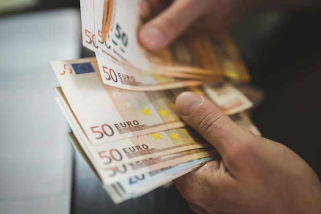 Biznesmen liczenia pieniędzy. bogate męskie dłonie trzymają i liczą banknoty 50 euro banknoty lub banknoty przed laptopem