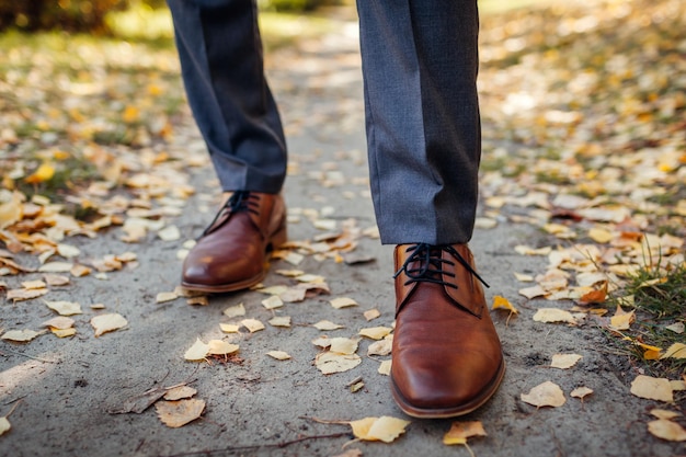 Biznesmen ma na sobie buty w jesiennym parku Brązowe skórzane obuwie klasyczne Strój pana młodego Zbliżenie nóg