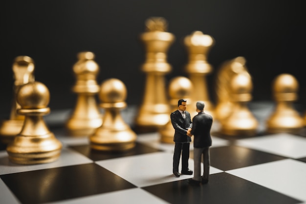 Zdjęcie biznesmen miniaturowy uścisk dłoni na szachownicy z złote szachy.