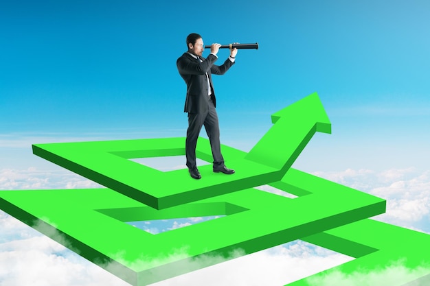 Zdjęcie biznesmen na abstrakcyjnym zielonym labiryncie strzałek używający lornetki do patrzenia w odległość na tle nieba koncepcja wzrostu i badań