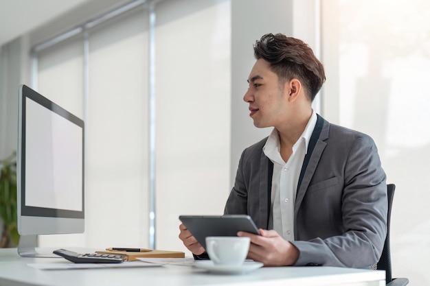 Biznesmen patrząc na monitor komputera trzymając tabletkę siedzącą w biurze