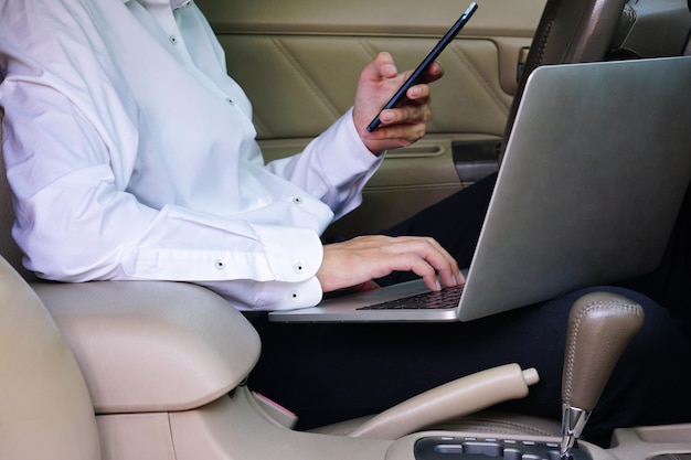 Biznesmen pracuje na laptopie i telefonie komórkowym, siedząc na siedzeniu kierowcy w samochodzie Koncepcja stylu życia