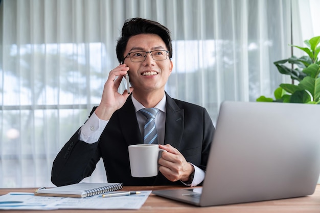 Biznesmen pracuje na laptopie przy biurku i rozmawia przez telefon Jubilant