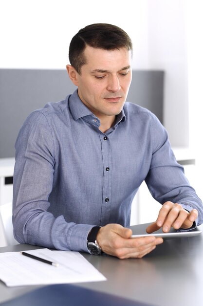 Biznesmen pracy z komputerem typu tablet w nowoczesnym biurze. Headshot męskiego przedsiębiorcy lub dyrektora firmy w miejscu pracy. Pomysł na biznes
