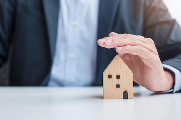 Biznesmen ręcznie pokrywa drewniany model domu ubezpieczenia nieruchomości i koncepcje majątkowe