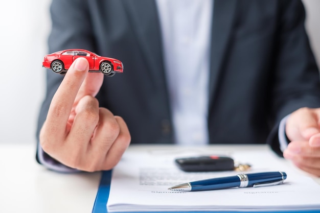 Biznesmen ręka trzyma czerwony samochód zabawka z bezkluczykowym długopisem pojazdu i dokumentem umowy kupna i sprzedaży ubezpieczenia koncepcje umowy najmu i umowy