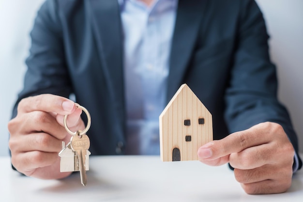 Biznesmen ręka trzyma klucz z drewnianym Model domu Kupno i sprzedaż nieruchomości Koncepcje umów najmu i umowy ubezpieczenia nieruchomości