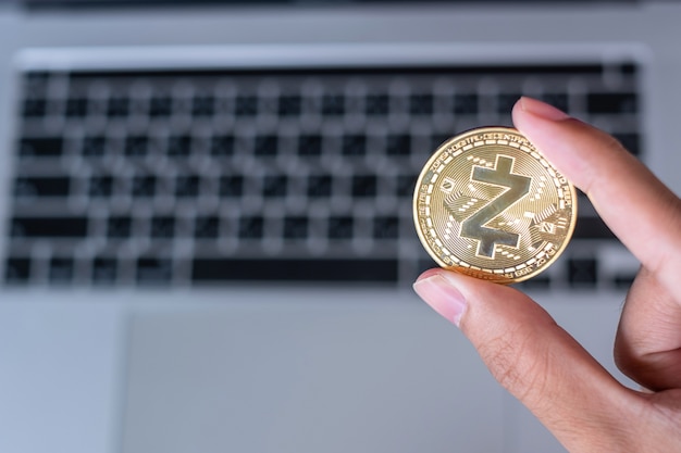 Biznesmen ręka trzymająca złotą monetę kryptowaluty Zcash (ZEC) na klawiaturze laptopa, Crypto to cyfrowe pieniądze w sieci blockchain, korzysta z technologii i internetowej wymiany internetowej.
