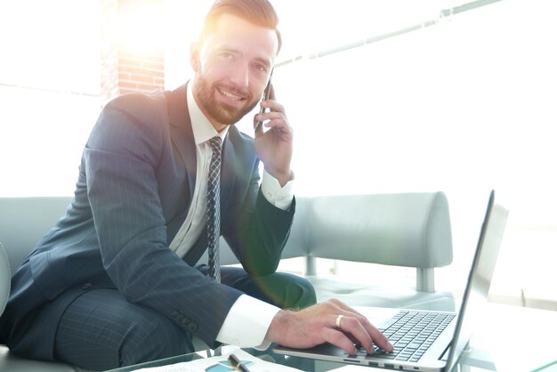 Biznesmen rozmawia na smartfonie i wpisuje tekst na laptopie