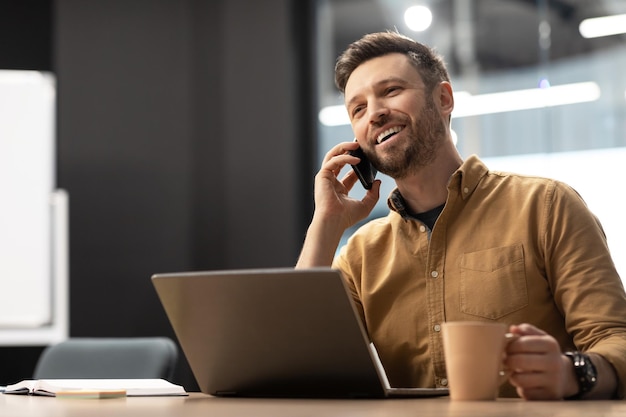 Biznesmen rozmawia przez telefon za pomocą laptopa siedzącego w miejscu pracy