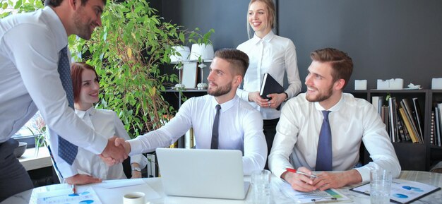 Biznesmen ściska ręce, aby przypieczętować umowę ze swoim partnerem i współpracownikami w biurze