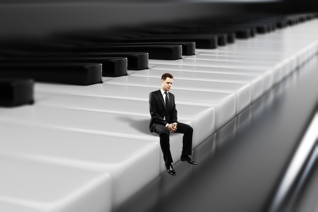 Biznesmen siedzący na klawiszach fortepianu