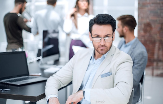 Biznesmen siedzący przy biurku na tle biurowych ludzi biznesu