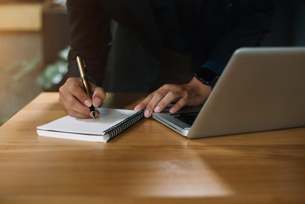 Biznesmen siedzi przy stole w domu, pracuje na laptopie i zapisuje pomysły w zeszycie