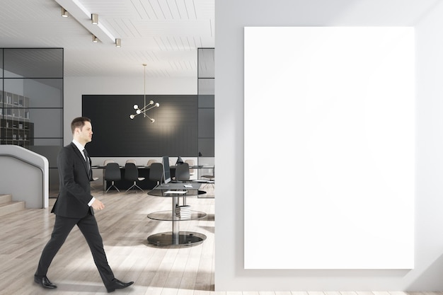 Biznesmen spacerujący w nowoczesnym wnętrzu sali konferencyjnej z pustym plakatem makieta duży stół drewniane podłogi sprzęt szklane okna i światło słoneczne