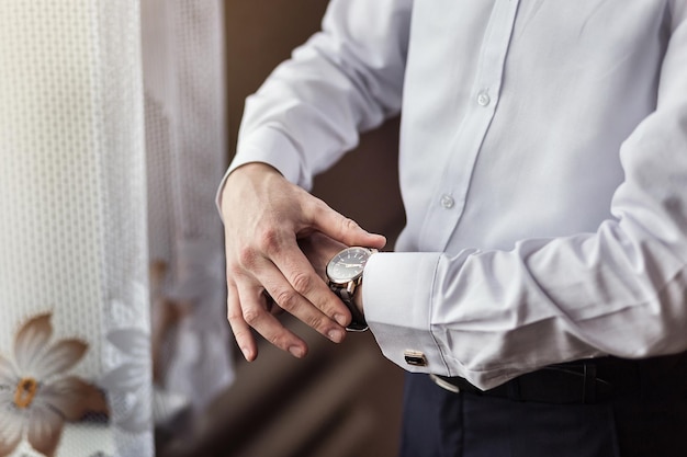 Biznesmen sprawdzający czas na swoim zegarku mężczyzna stawiający zegar na pana młodego szykuje się rano przed ceremonią ślubną