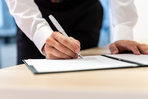 Biznesmen stojąc przy biurku, podpisując raport lub umowę z atramentem pióra.