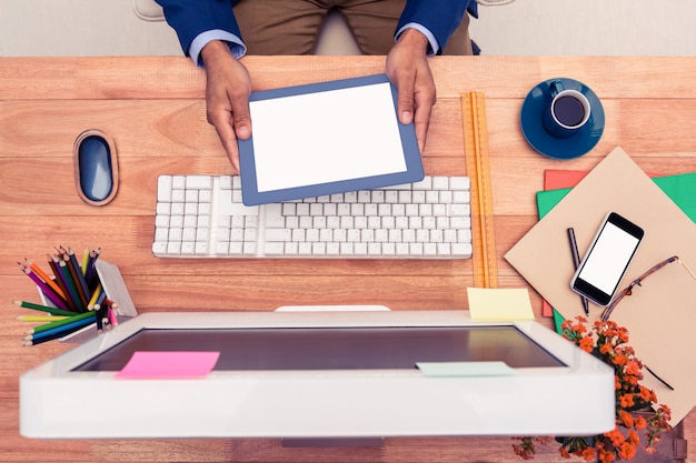 Biznesmen trzyma cyfrową pastylkę podczas gdy siedzący przy komputerowym biurkiem w kreatywnie biurze