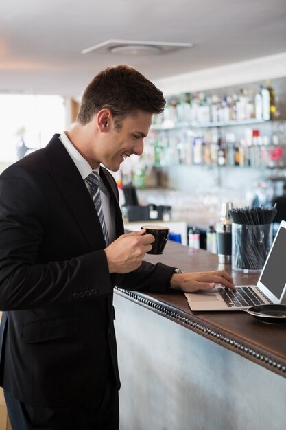 Biznesmen trzyma filiżankę kawy podczas gdy używać laptop