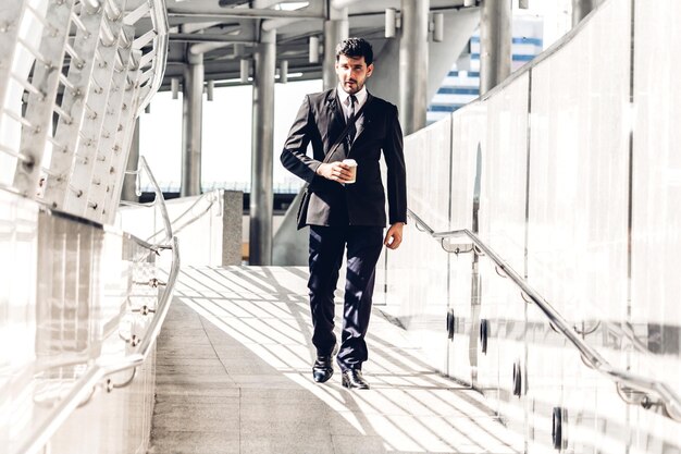 Zdjęcie biznesmen trzymający jednorazowy kubek idący po mostku