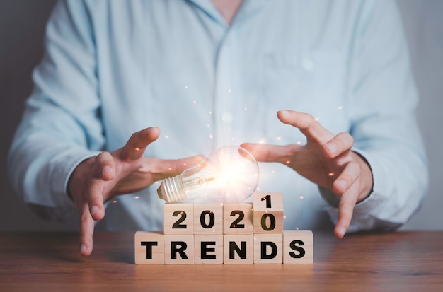 Biznesmen trzymający żarówkę podczas przerzucania trendów z lat 2020-2021, drukując ekran na drewnianych kostkach.