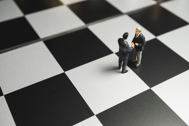 Zdjęcie biznesmen uścisk dłoni miniaturowy na tle szachownicy. koncepcja partnerstwa.
