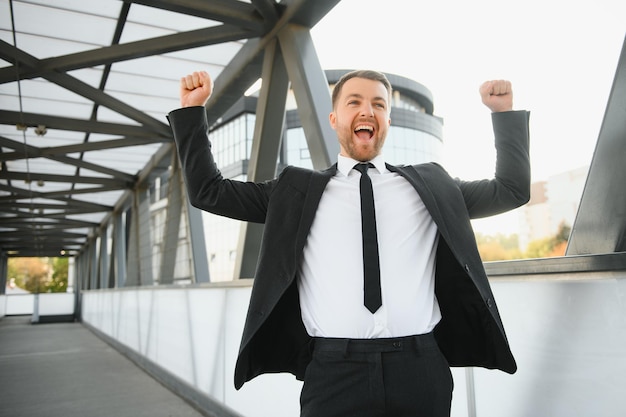 Zdjęcie biznesmen uśmiecha się i podnosi pięść w powietrzu z biurem w tle, osiąganie sukcesu w biznesie i wygrywanie koncepcji