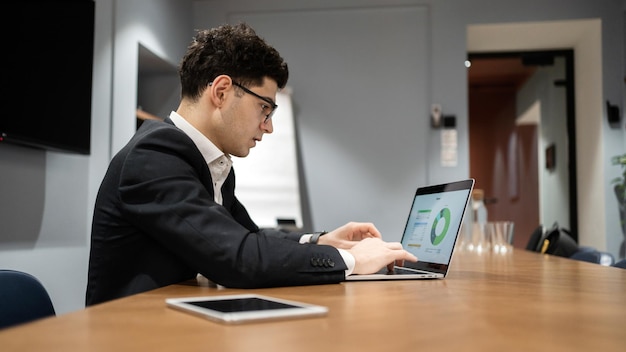 Biznesmen używa laptopa, młodego, odnoszącego sukcesy przedsiębiorcy, samotnie w biurze pracującym w formalnym